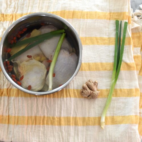 Preparation for instant pot herbal chicken soup: raw chicken thighs in an Instant Pot bowl with water, ginger, scallion, and traditional herbs on the side.