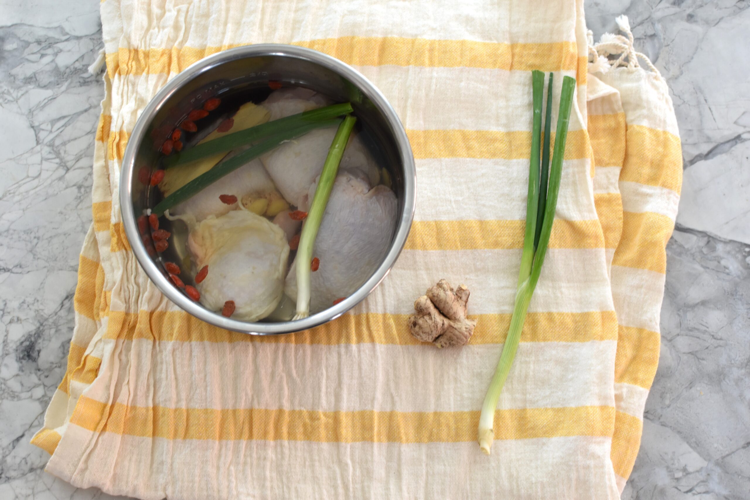 Preparation for instant pot herbal chicken soup: raw chicken thighs in an Instant Pot bowl with water, ginger, scallion, and traditional herbs on the side.