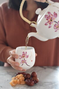 woman pouring longan red date tea from teapot into cup.